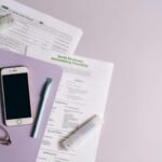 Flat lay of accounting documents, smartphone, and glasses on a desk.