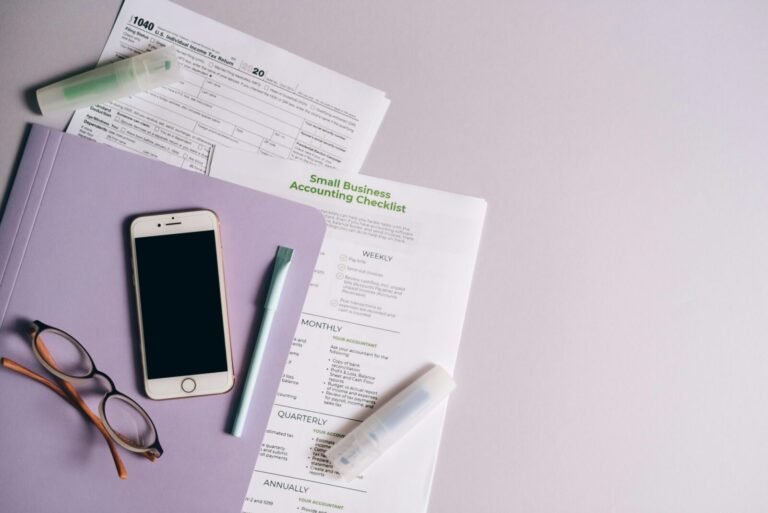 Flat lay of accounting documents, smartphone, and glasses on a desk.